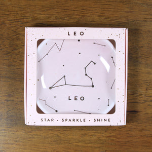 Leo Zodiac Ring Dish from Lucky Feather. Blush blue colored ring dish with gold print. Ring dish says Leo and has an illustration of the Leo constellation.