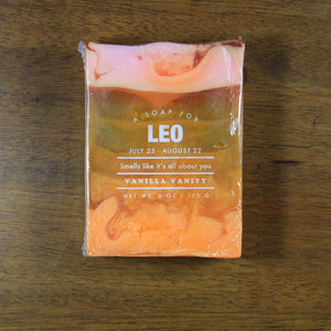 Whiskey Rivers Soap Co. Leo Astrology Soap. The bar is translucent orange with opaque orange on the bottom and pink swirled into the top. In white writing, says "a soap for Leo. July 23-August 22. Smells like it’s all about you. Vanilla Vanity."