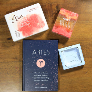 flat lay of what's your sign aries zodiac gift box contents: aries zodiac crystals, aries soap, aries book and aries ring dish on wood table