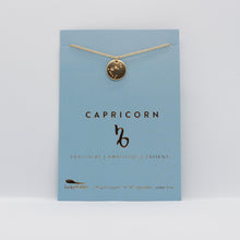 Load image into Gallery viewer, Capricorn Zodiac Necklace by Lucky Feather. A gold disc necklace with the Capricorn constellation etched in it, on a blue paper board.
